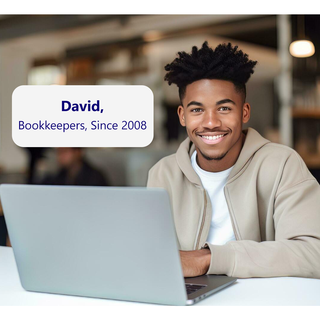 A QuickBooks bookkeeper named David is sitting at a desk and smiling. 